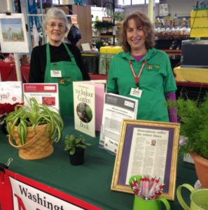 two women stand behind display table with herbs and vegetables