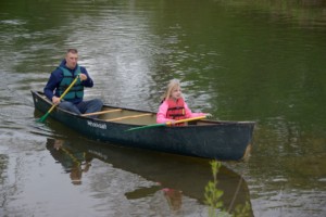 father and daughter in canoe wearing life jakcets and paddling on creek