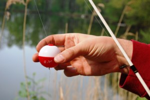 hand holding fishing bob and pole over water