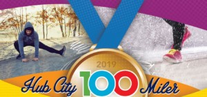 male stretching in running gear, shoes running with snow, gold medal with words: 2019 Hub City 100 Miler